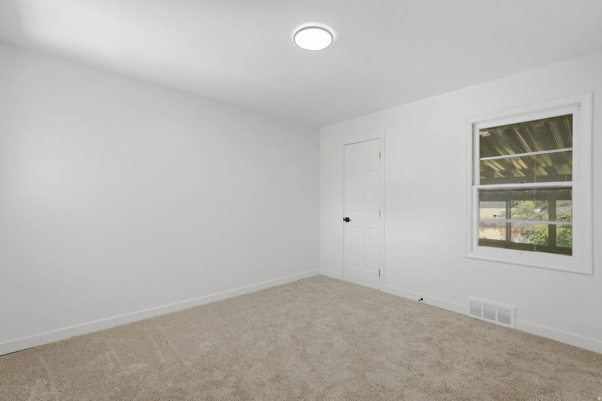 Carpeted room featuring a white paneled door with matte black hardware, a double-hung window, and a ceiling-mounted flush light fixture