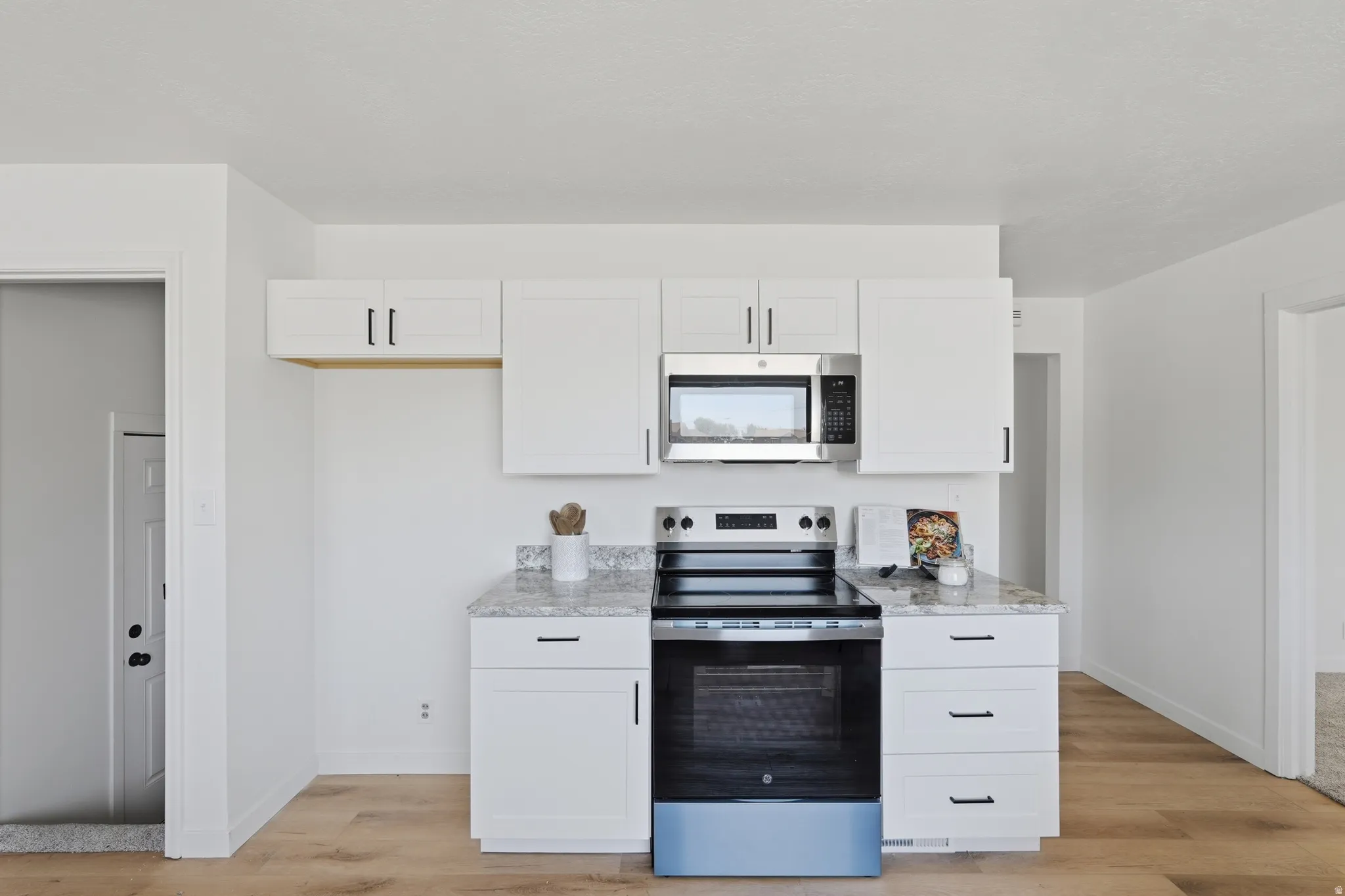 Contemporary kitchen featuring white cabinetry, stainless steel appliances, granite-style countertops, and wood-finish flooring