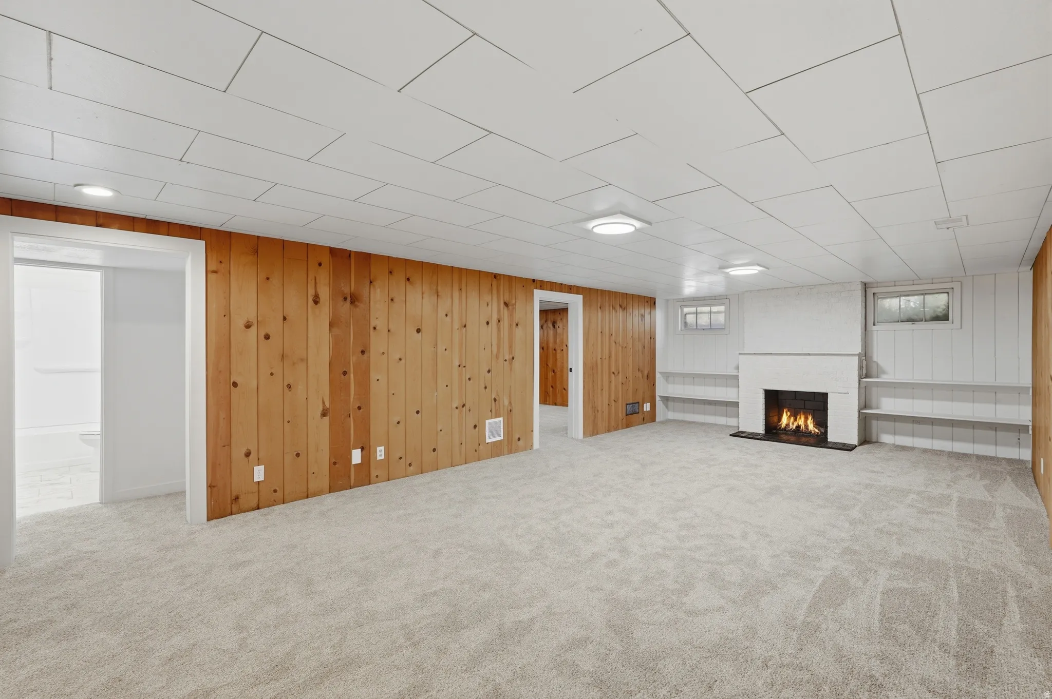 Finished lower-level space featuring light-toned carpet, recessed lighting, and a white ceiling with a geometric panel pattern