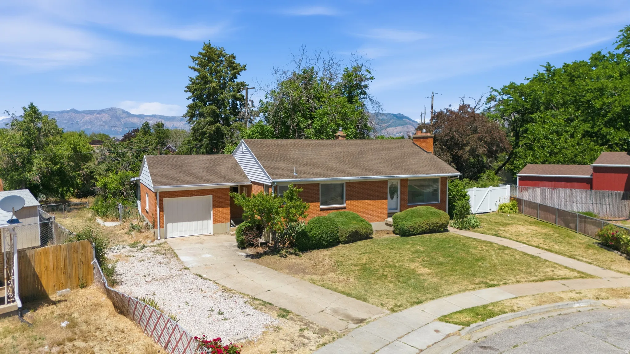 Brick exterior ranch home with an attached garage, a paved driveway, and established front landscaping