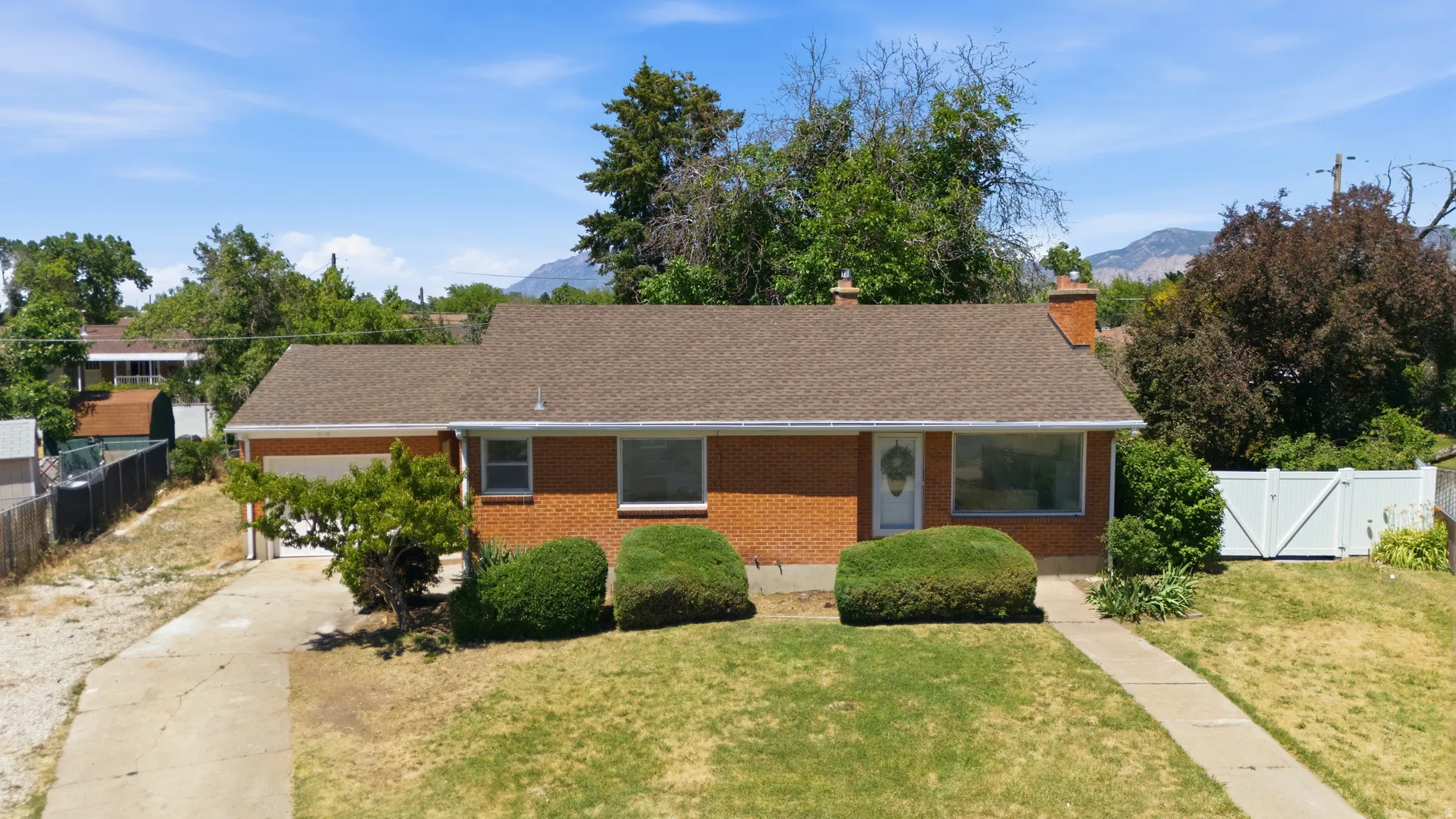Brick exterior home featuring a brown shingle roof, attached garage, concrete driveway, and front lawn