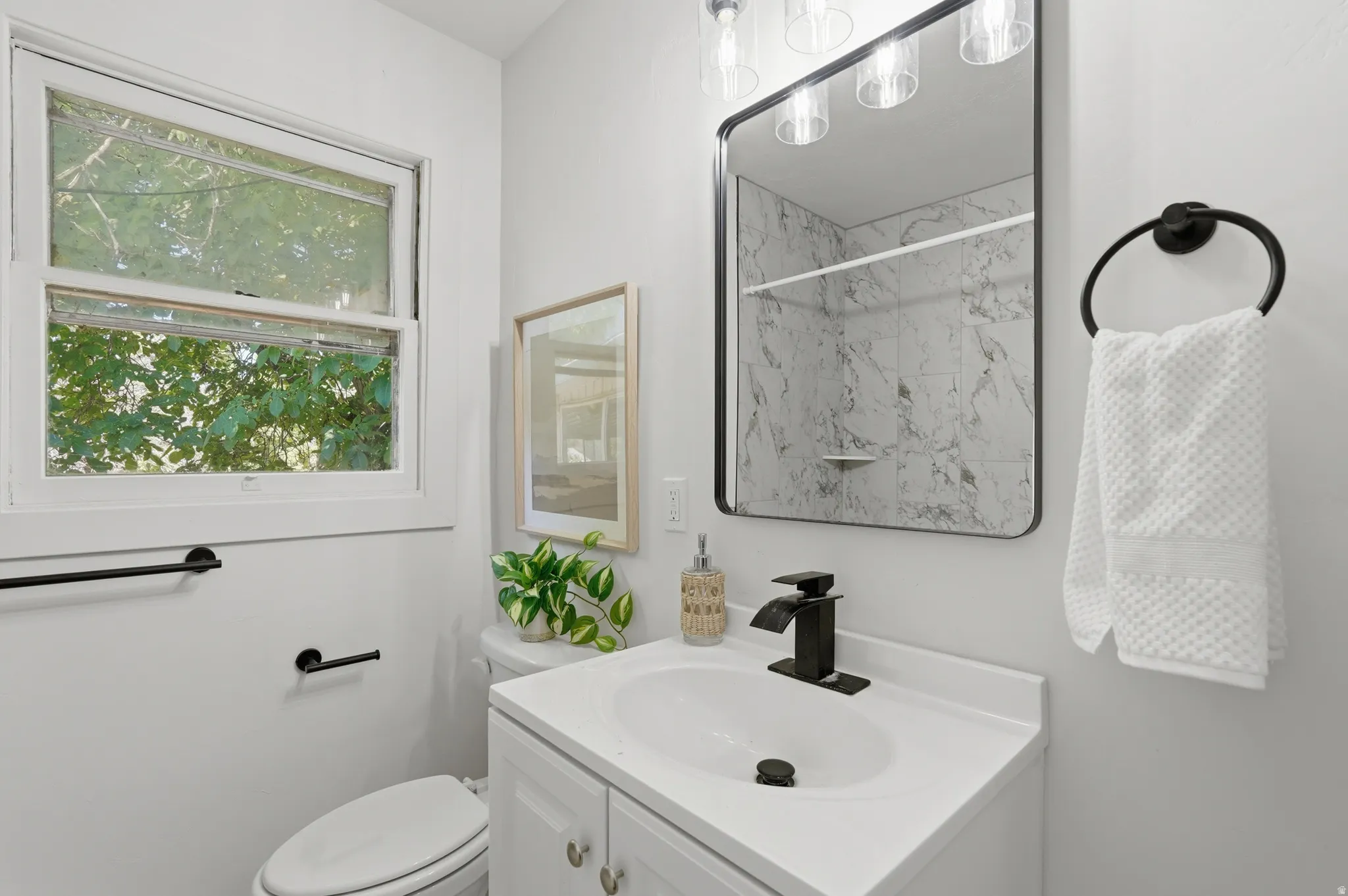 Bathroom featuring a white vanity with integrated sink, black hardware, framed mirror, and window