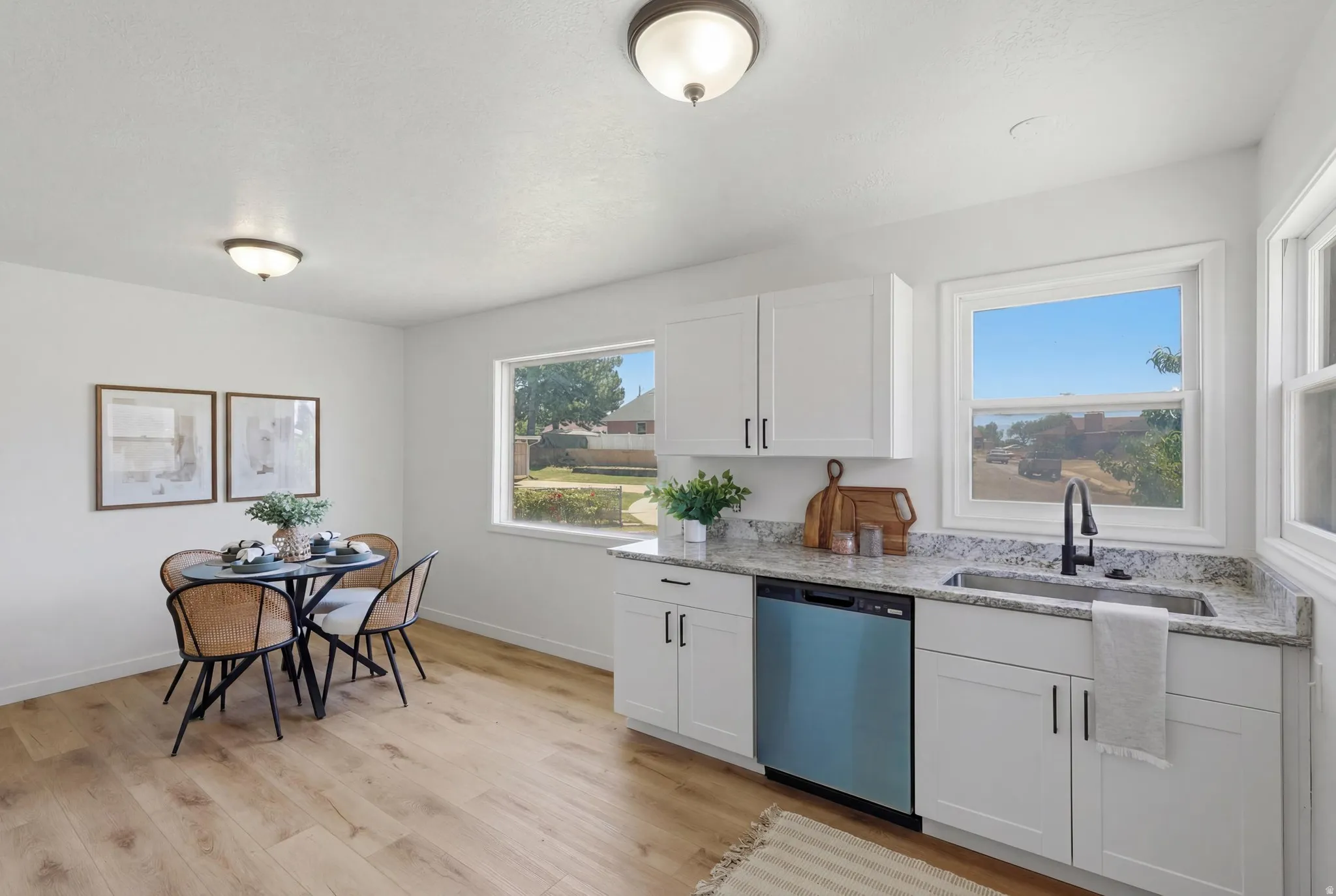 Bright kitchen featuring white shaker cabinetry, granite-style countertops, a stainless steel sink with a matte black faucet, and modern wood-finish flooring