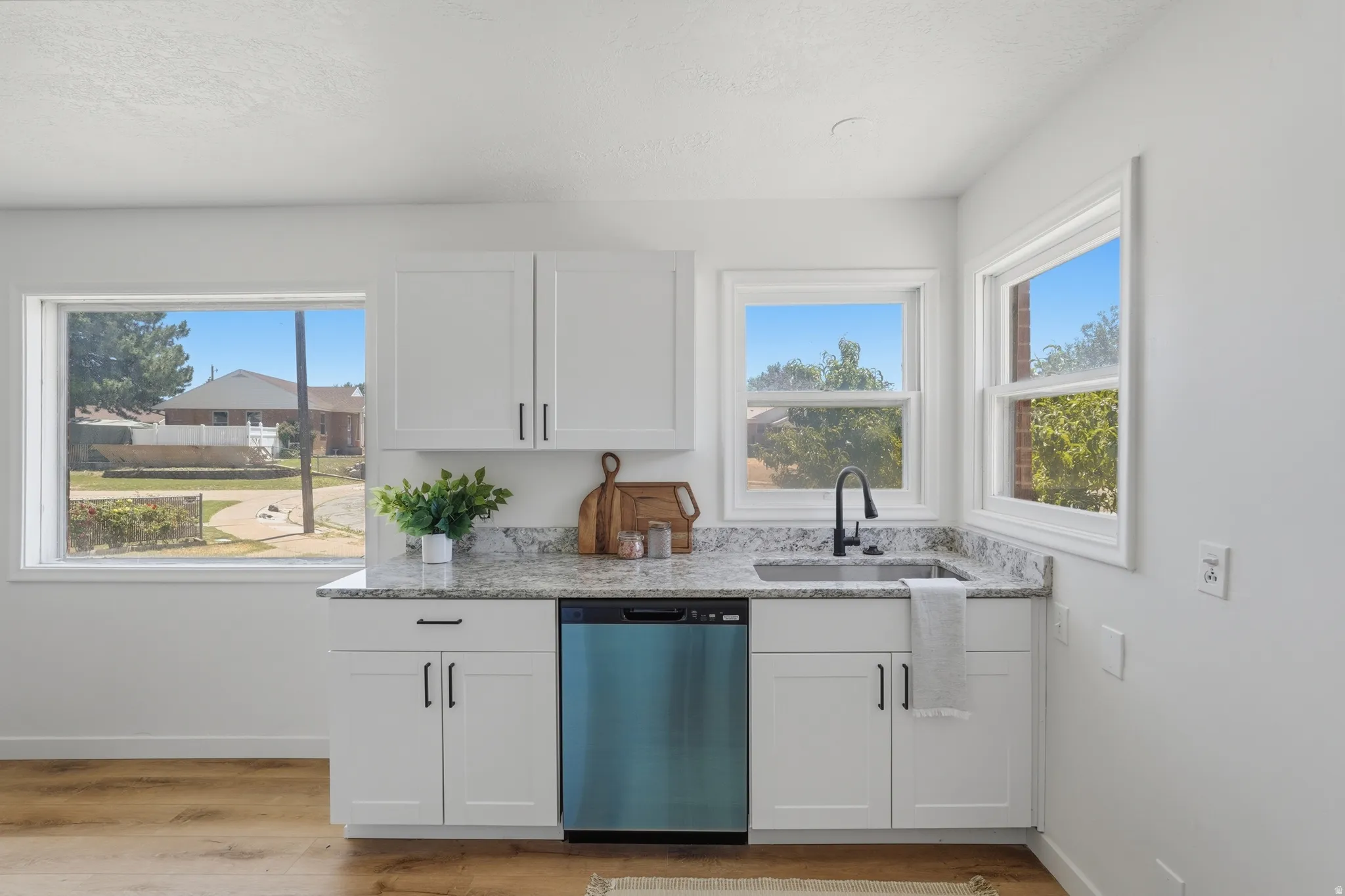 Kitchenette featuring white shaker cabinetry, speckled countertop, stainless steel sink with a matte black faucet, and a panel-ready dishwasher