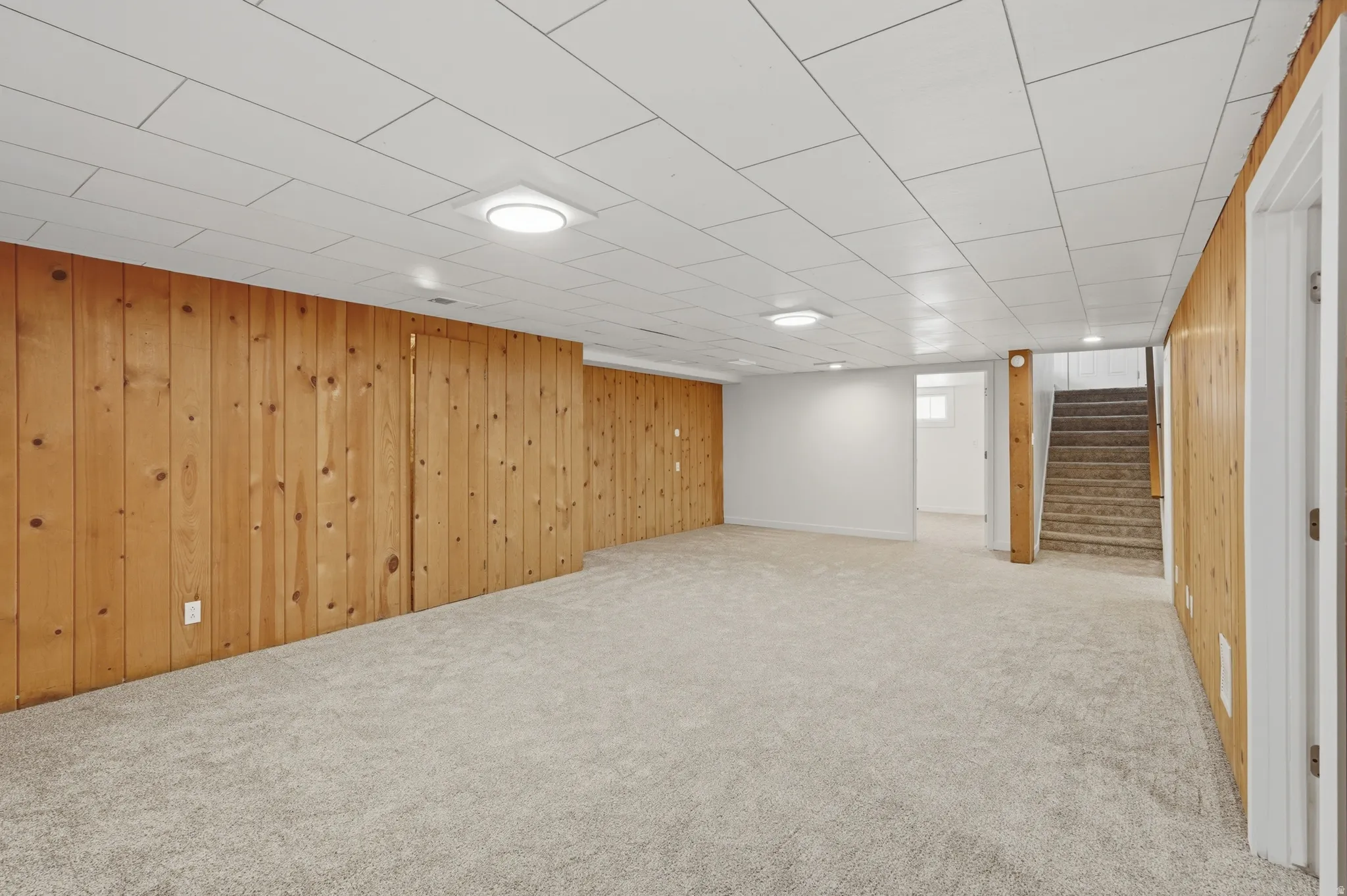 Spacious room featuring light-colored carpeting, wood paneling, white walls, and a white tile ceiling with recessed lighting