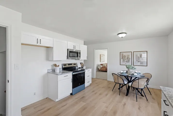 Kitchen and dining area featuring white cabinetry, stainless steel microwave, black range, and light wood-finish flooring