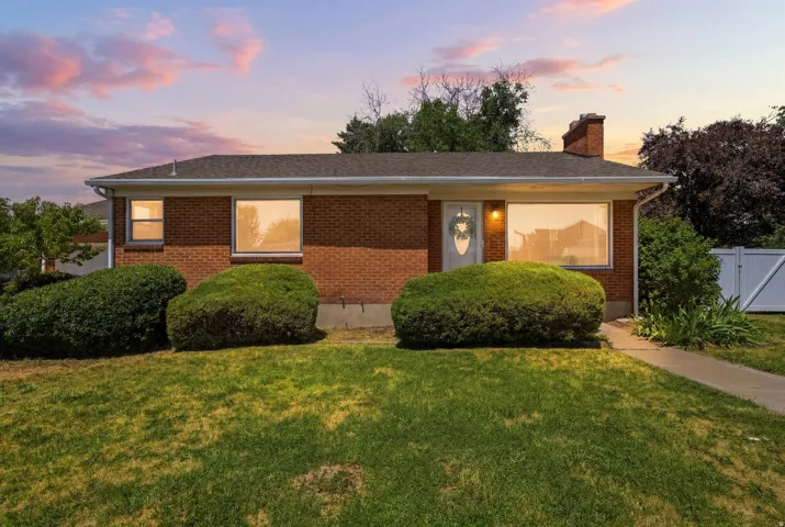 Brick exterior with a gabled roofline, front lawn, and mature shrubbery