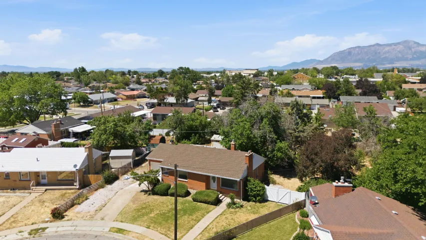 Aerial perspective of a neighborhood featuring multiple residential properties with pitched roofs, mature trees, and mountain scenery in the distance