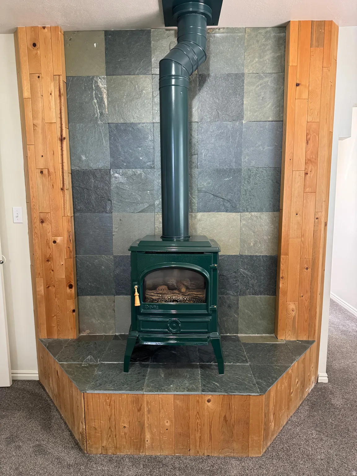Freestanding green fireplace with an exposed flue, set against a slate tile wall