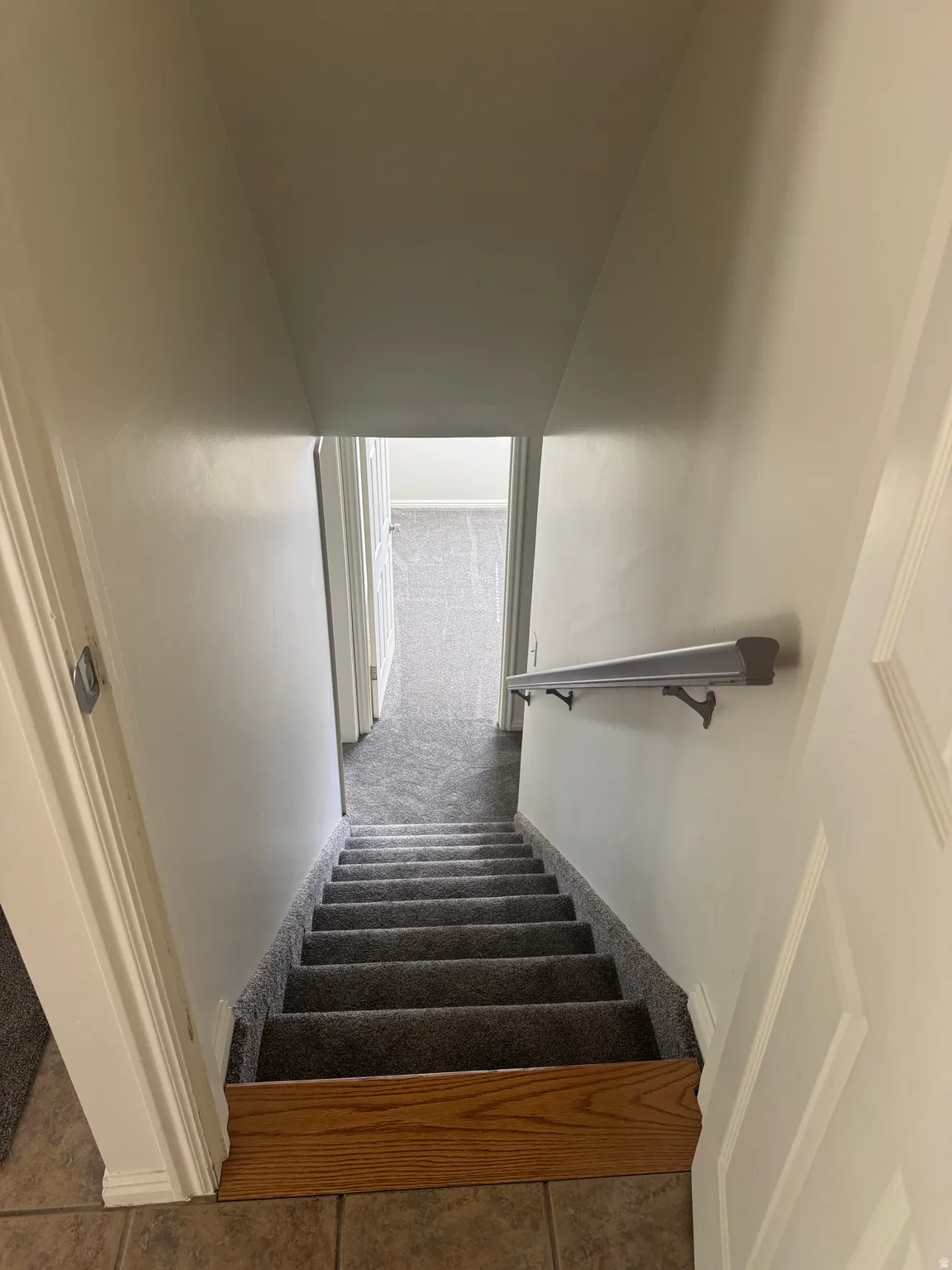 Carpeted staircase with light gray carpeting and a wood-finish baseboard, complemented by a wall-mounted handrail