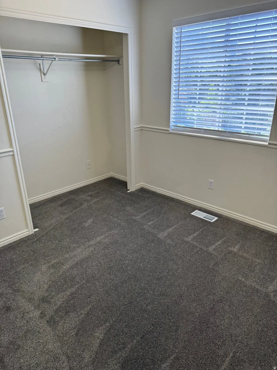 Interior room featuring plush gray carpeting, white walls, and a window with blinds