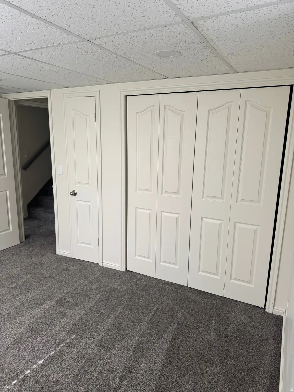 Recessed lighting illuminating a plush gray carpeted room with white bi-fold closet doors and a white paneled door