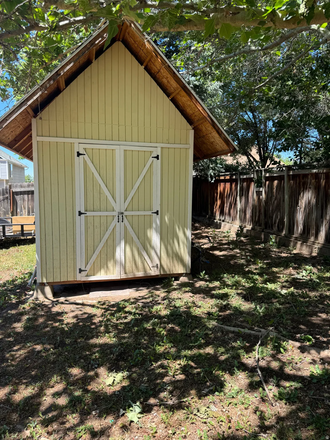 Gable-roof storage shed with light yellow siding and white double doors featuring cross-buck detailing