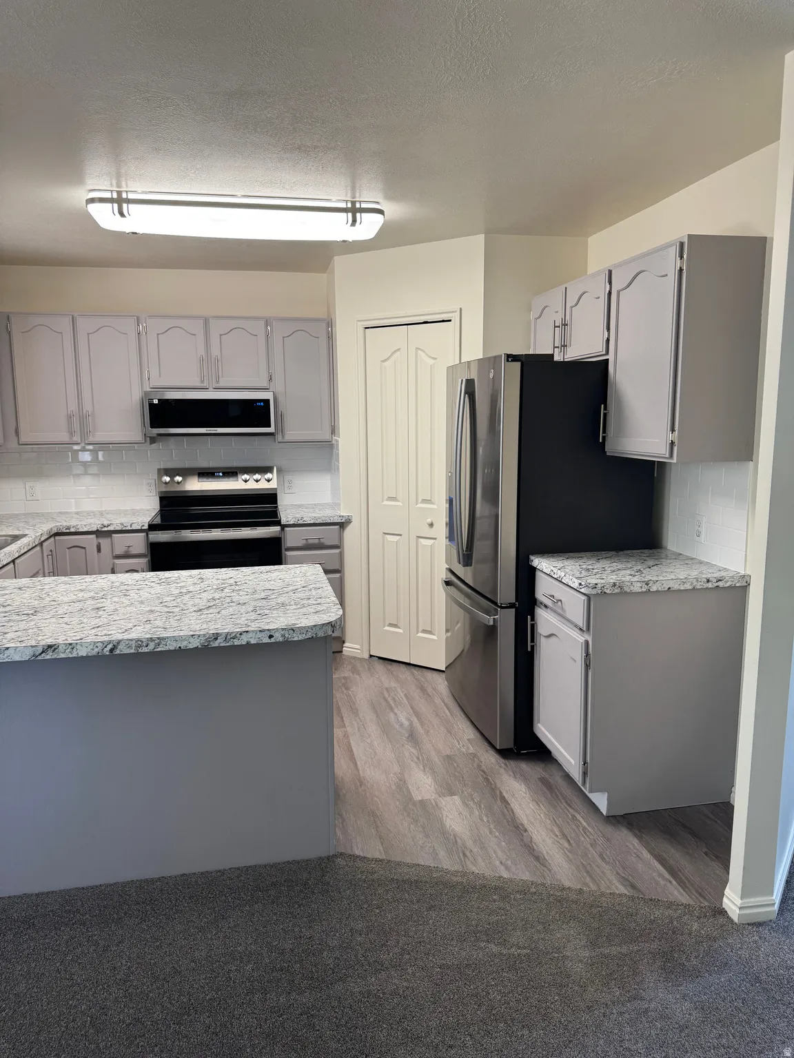 Kitchen featuring granite-style countertops, grey cabinetry, stainless steel appliances, and wood-finish flooring