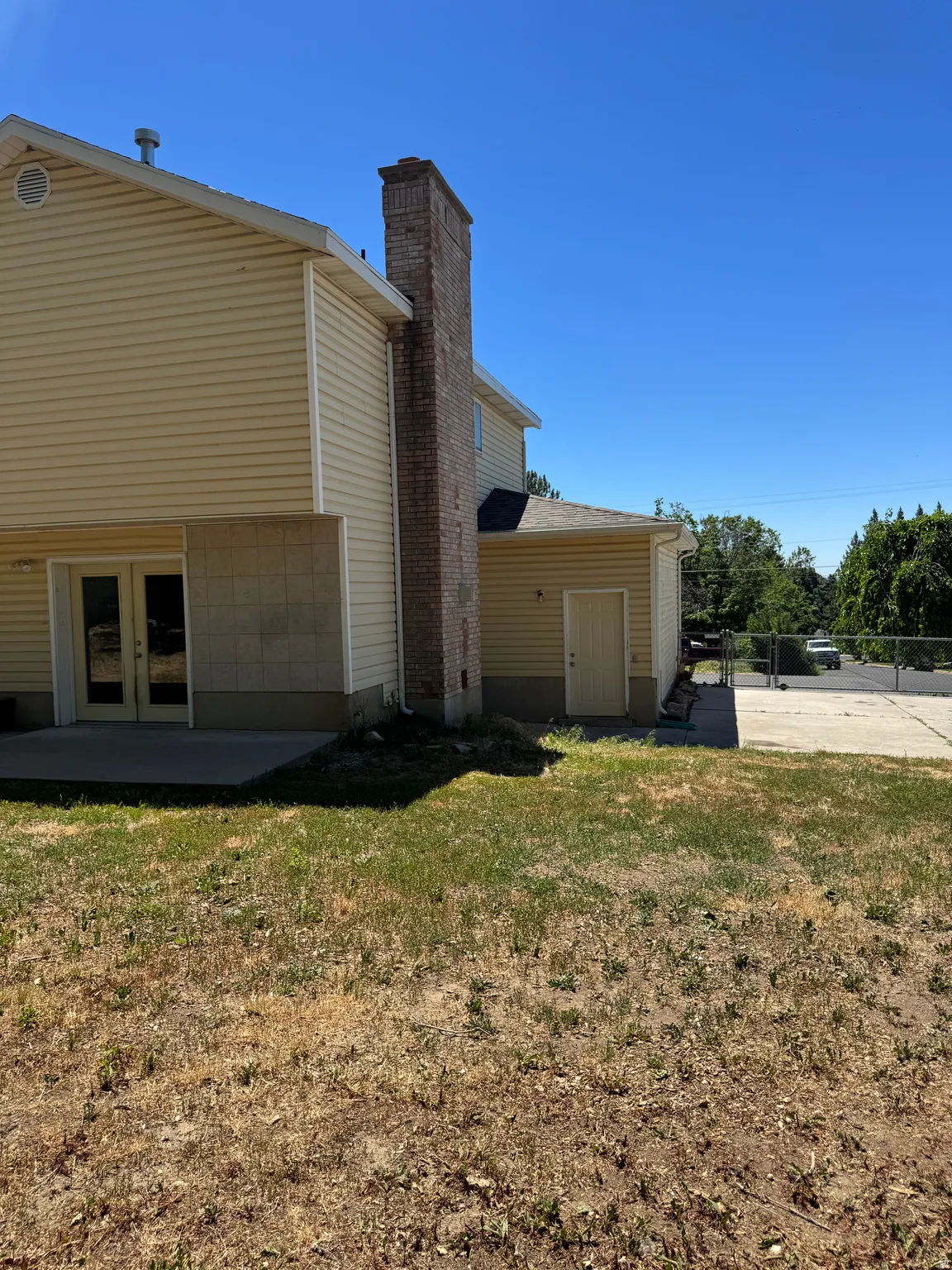 Rear exterior featuring light-colored siding, a prominent brick chimney, and a concrete patio