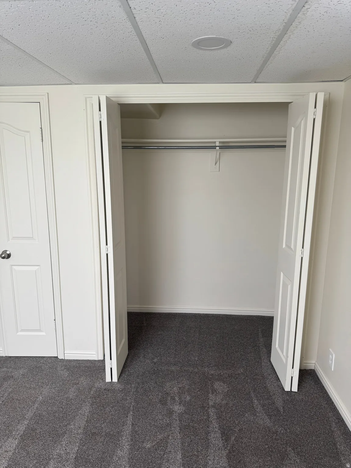 Integrated closet featuring bi-fold panel doors, white interior walls, and a hanging rod
