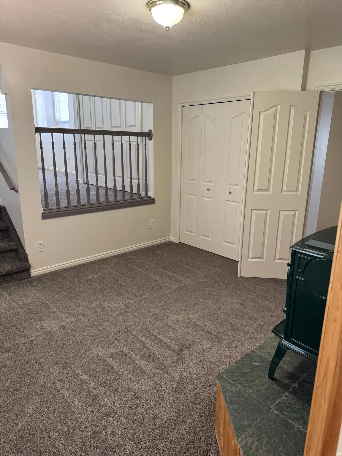 Carpeted interior space featuring a partial wall with a wood-tone railing and a built-in wood stove with a stone-tile base