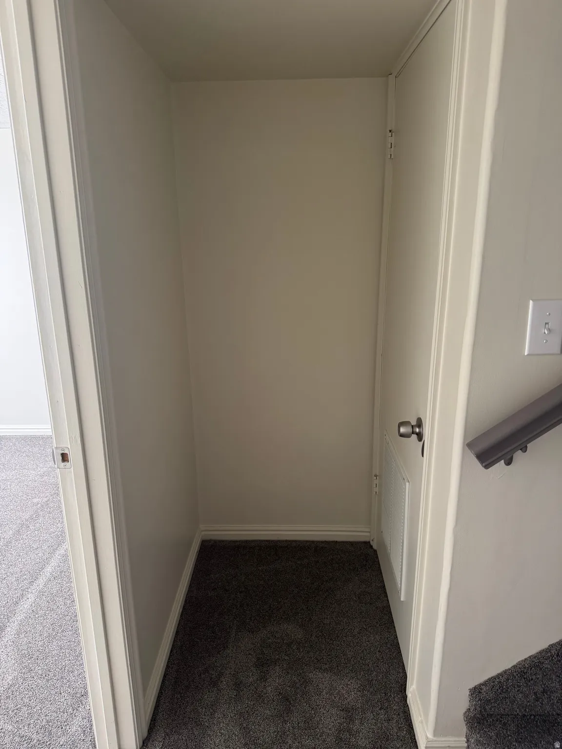 Recessed alcove with dark grey carpet flooring, white baseboards, and light neutral walls