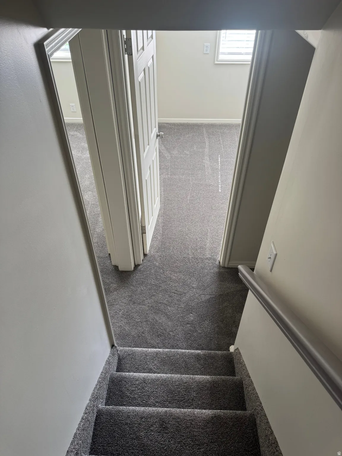 Carpeted staircase featuring a handrail, leading to a carpeted landing with two doorways