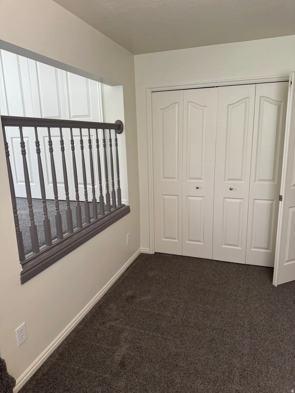 Carpeted space with bi-fold closet doors, white baseboards, and a dark gray balustrade