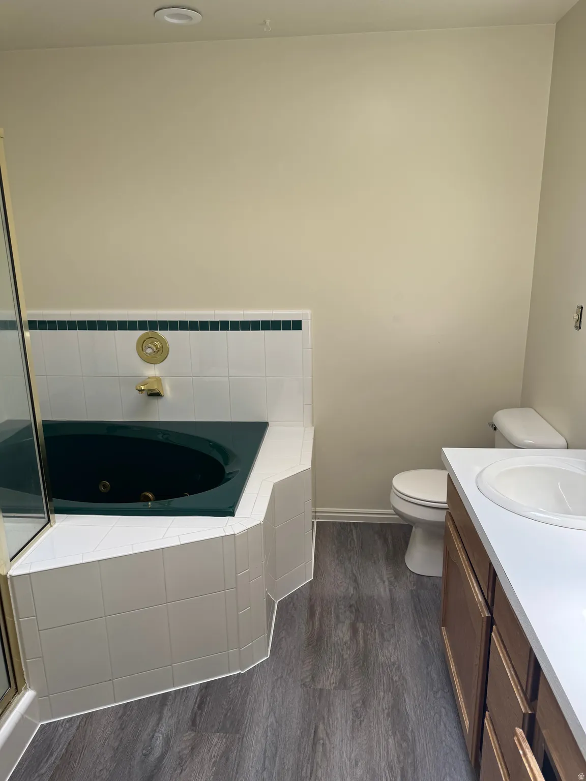 Corner soaking tub with white tile surround and green accent trim