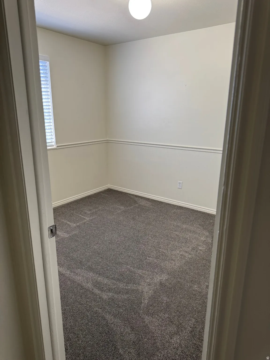 Room featuring light neutral wall colors, chair rail molding, wall-to-wall gray carpeting, a single window with horizontal blinds, and a ceiling-mounted light fixture