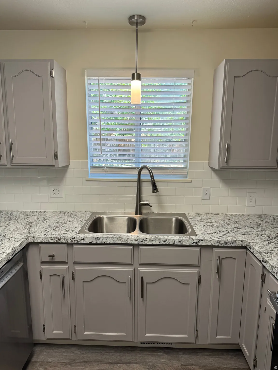 Kitchen featuring light gray cabinetry, a dual basin stainless steel sink, a dark finished faucet, white subway tile backsplash, and light-colored countertops