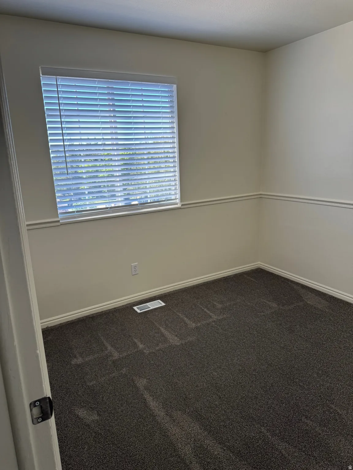 Carpeted room with a window featuring horizontal blinds