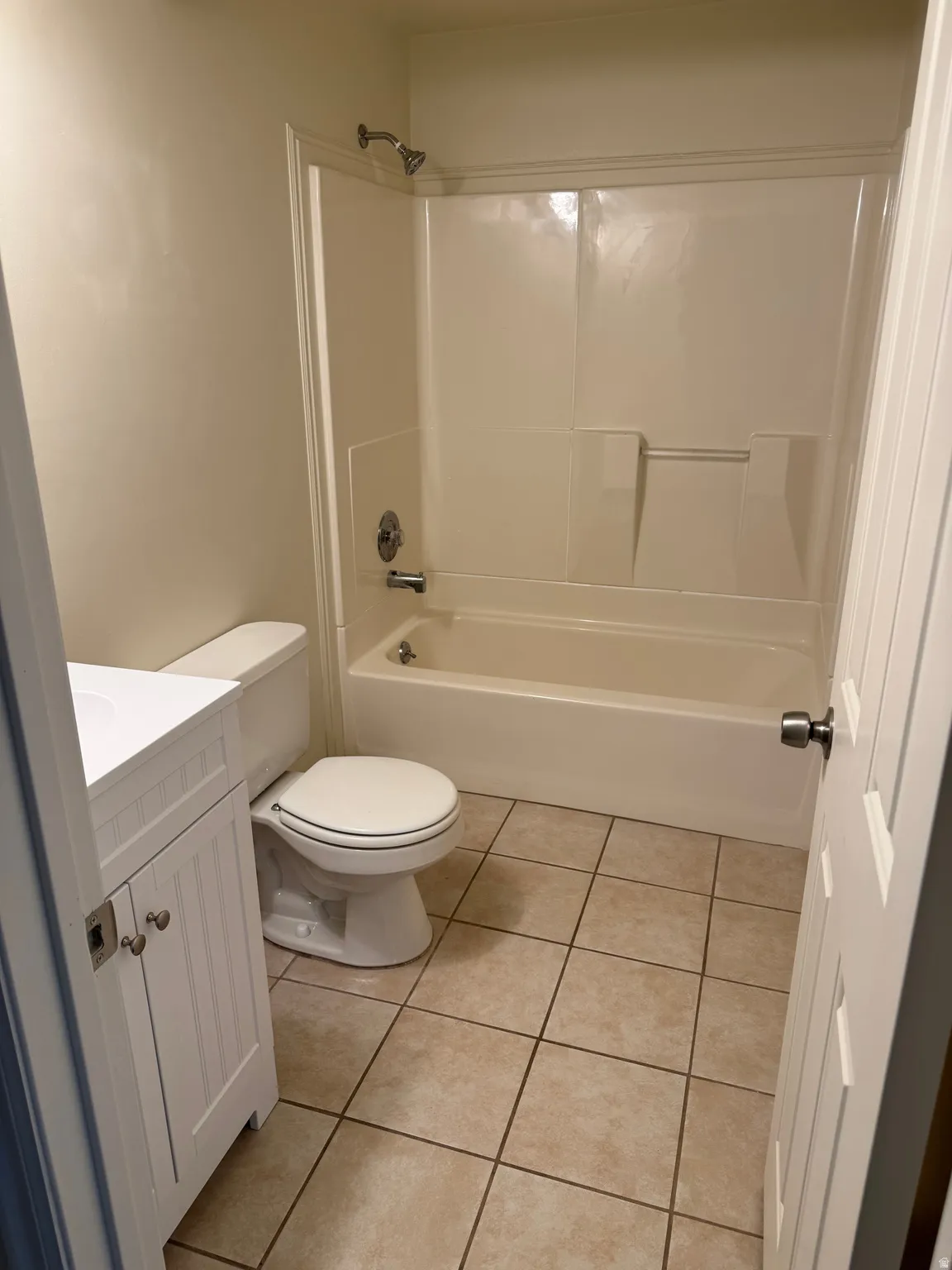 Bathroom featuring a white vanity with paneled doors, a white toilet, a bathtub with an integrated shower, and neutral-toned floor tiling