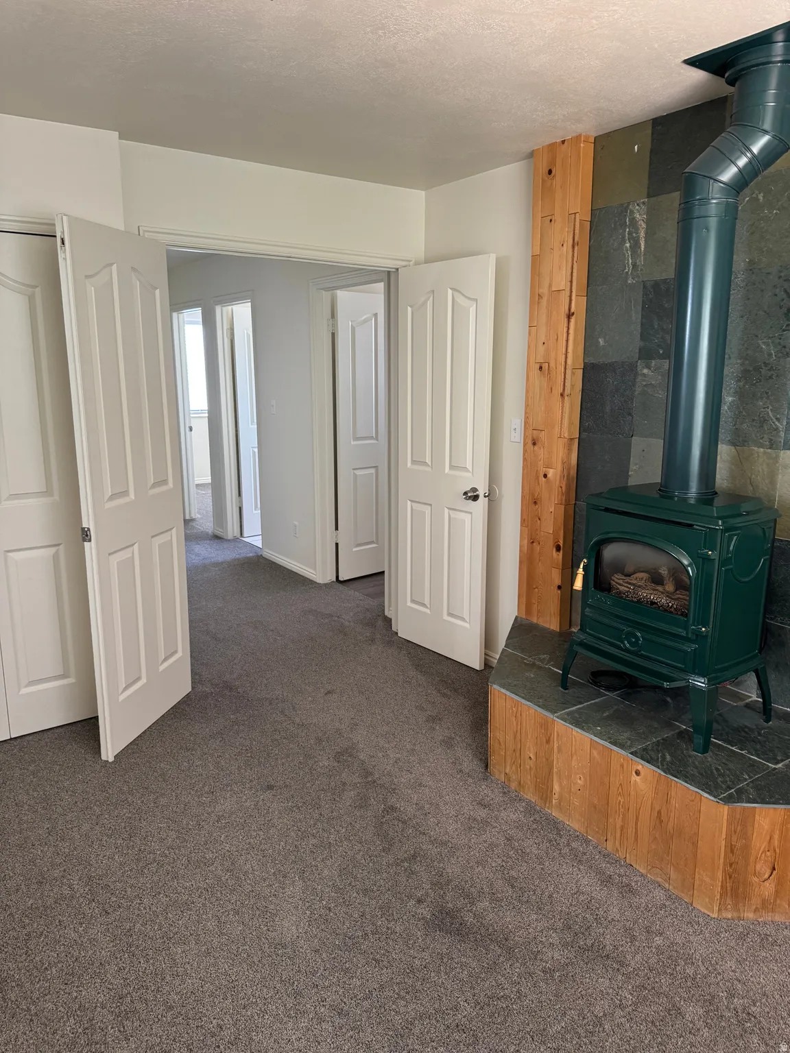 Freestanding wood-burning stove with a green finish, set on a slate hearth with a wood-paneled base