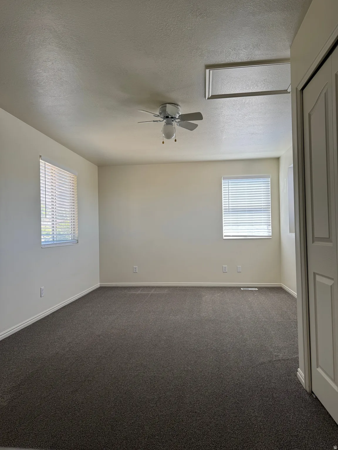 Spacious room featuring neutral carpeting, two windows with blinds, a ceiling fan with integrated lighting, and a white bi-fold closet door
