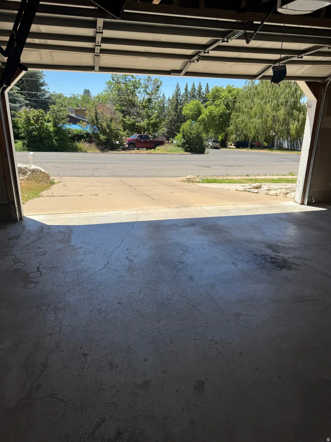 Garage interior with a concrete floor and an open overhead door, offering access to the exterior drive and street