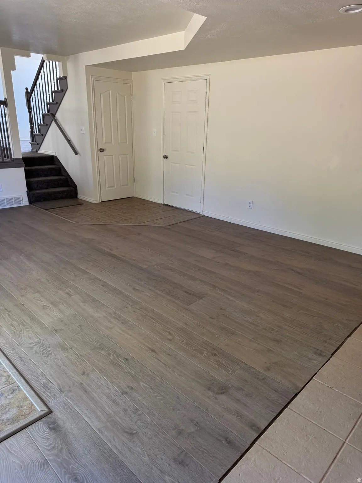Spacious interior featuring wood-finish flooring, a carpeted staircase with a dark wrought iron railing, and neutral wall tones