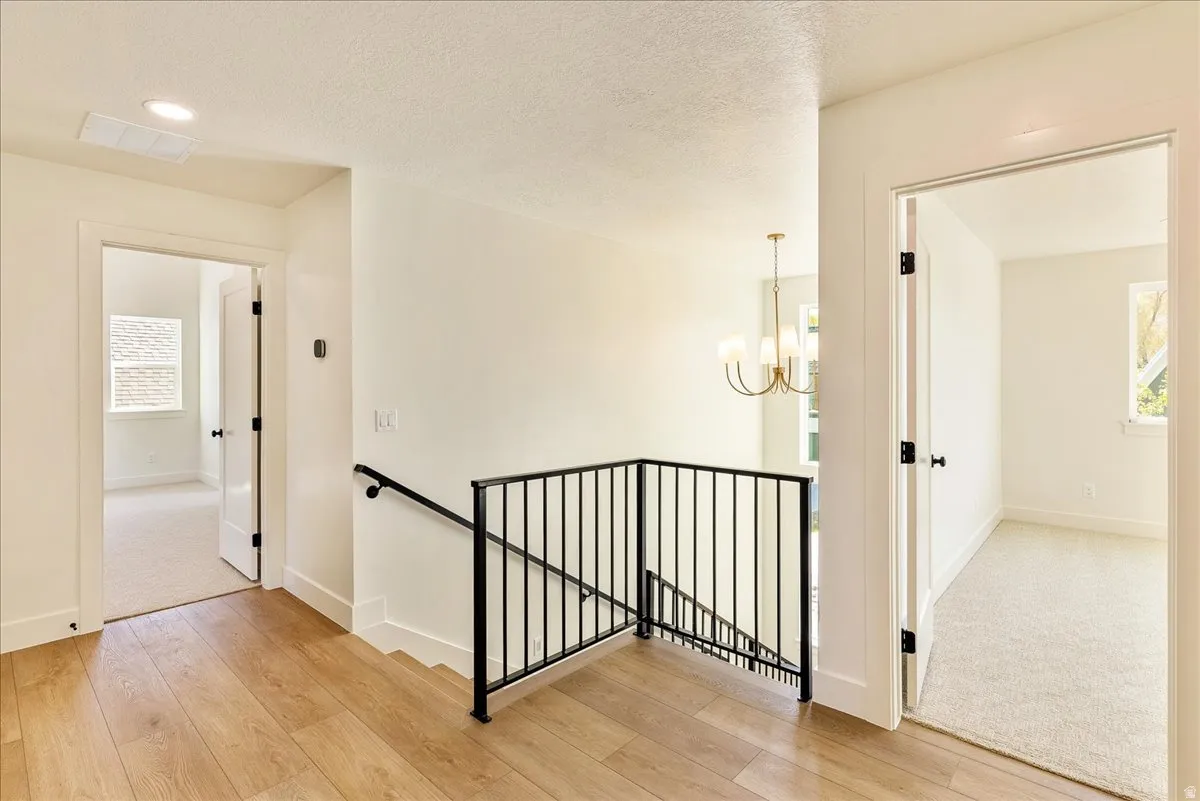 Upper-level hallway featuring wood-finish flooring, white walls, and a black wrought iron railing