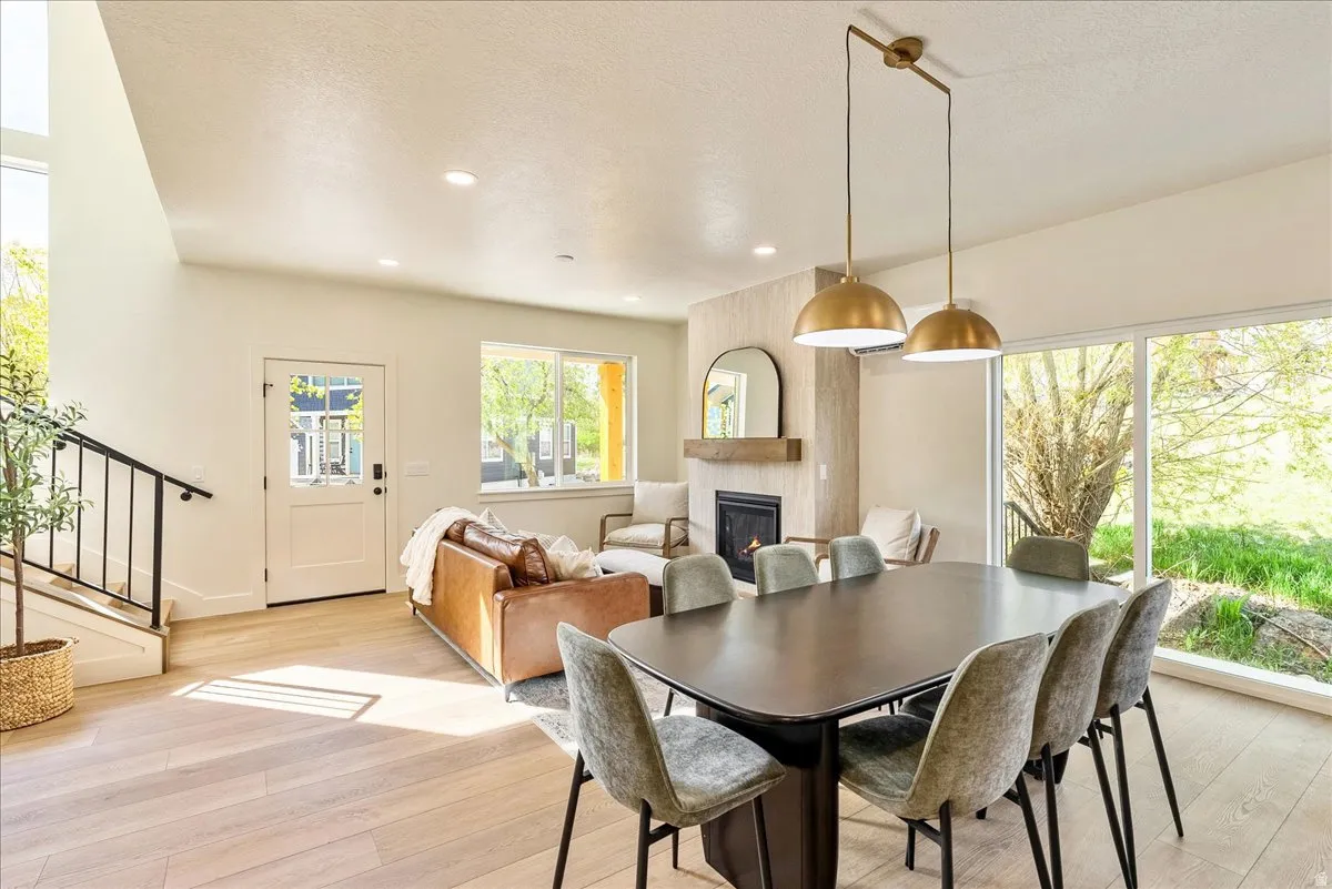 Open-concept living area with abundant natural light, wood-finish flooring, and a contemporary fireplace featuring a tile surround and wooden mantel
