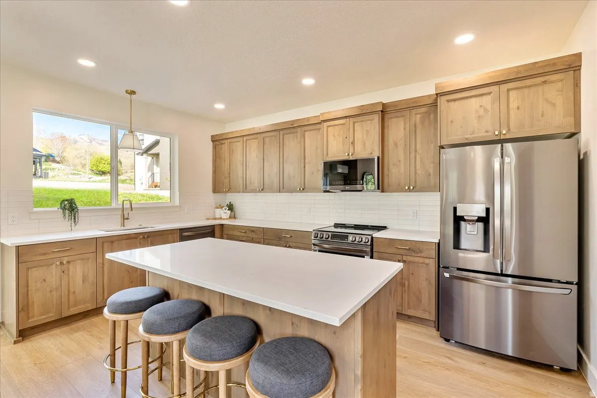 Kitchen featuring wood cabinetry, stainless steel appliances, white subway tile backsplash, white countertops, and wood-finish flooring