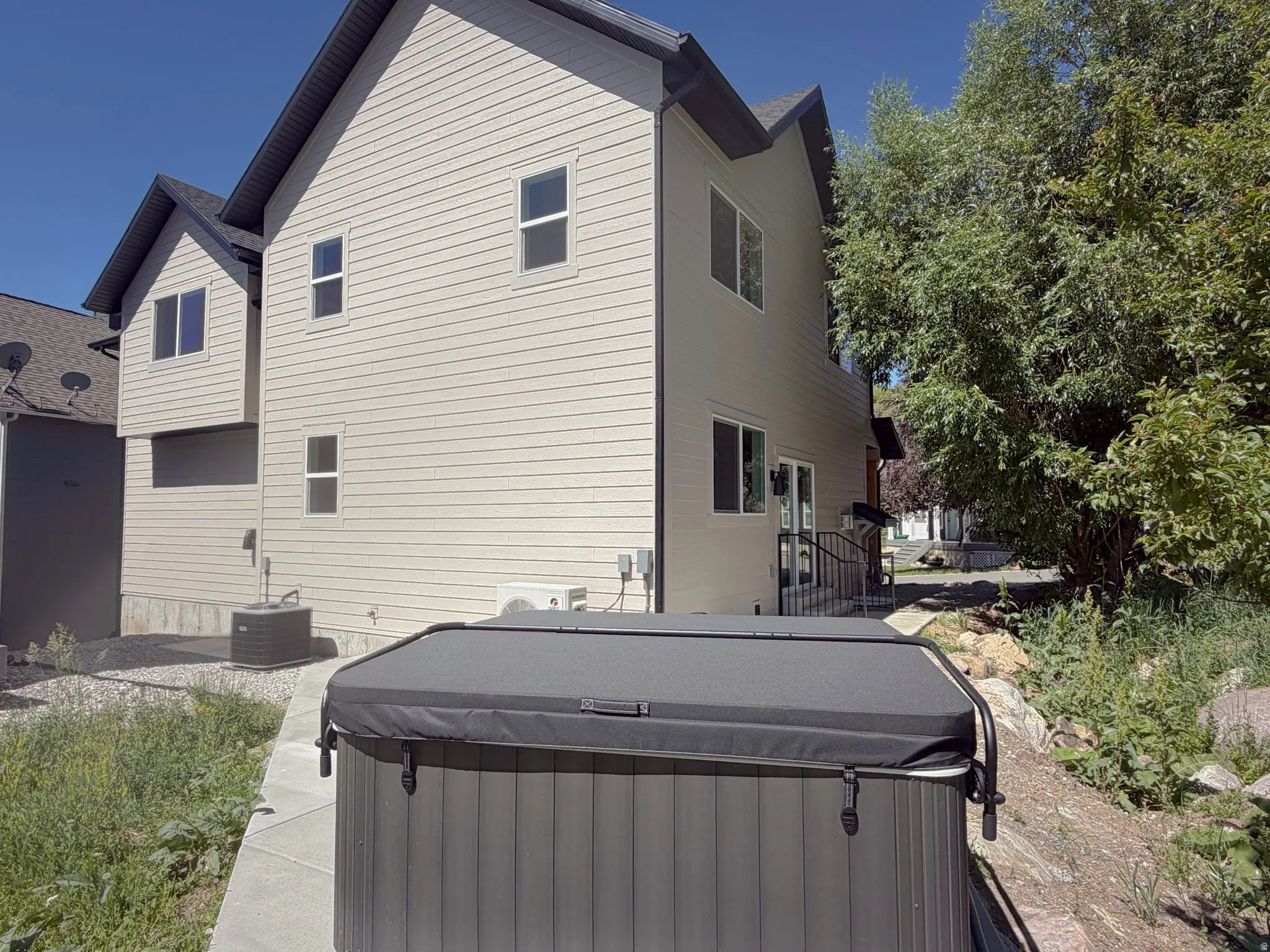 Rear exterior featuring light-colored siding, a covered hot tub, and mature trees