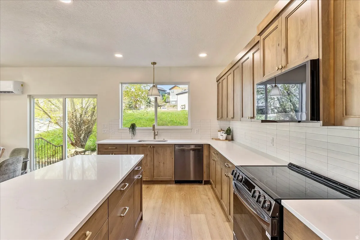 Spacious kitchen featuring light wood-finish cabinetry, white countertops, stainless steel appliances, and wood-finish flooring