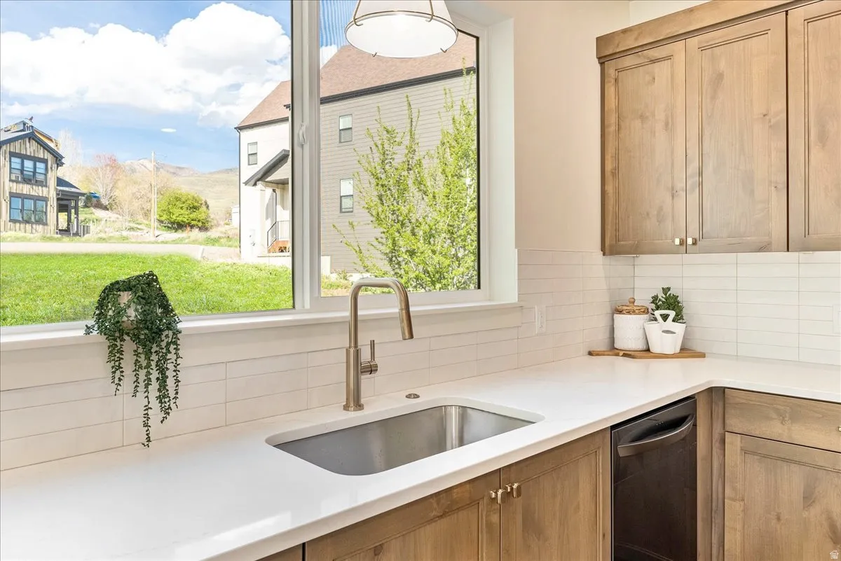 Kitchen featuring a stainless steel sink with a gooseneck faucet, light wood-finish cabinetry, a built-in dishwasher, white countertops, and a white subway tile backsplash