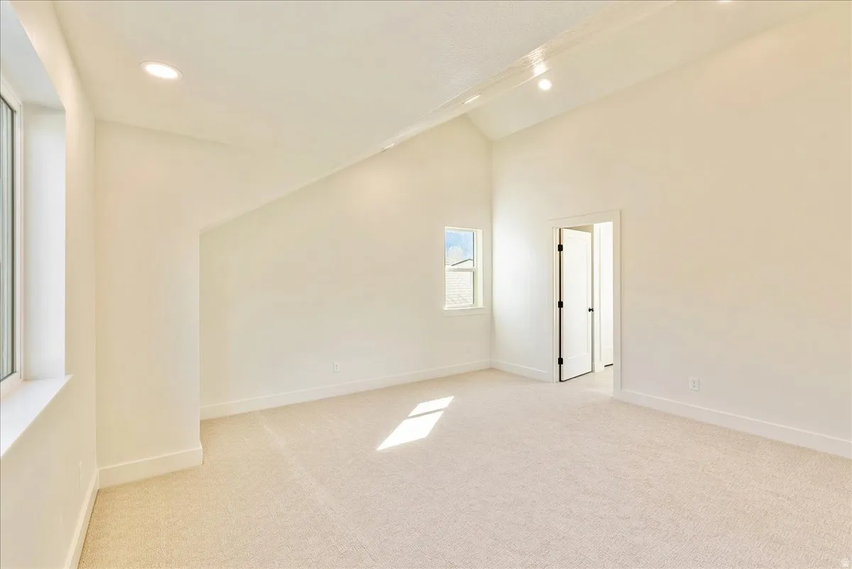Spacious room featuring vaulted ceilings, recessed lighting, neutral wall tones, plush carpeting, and multiple windows