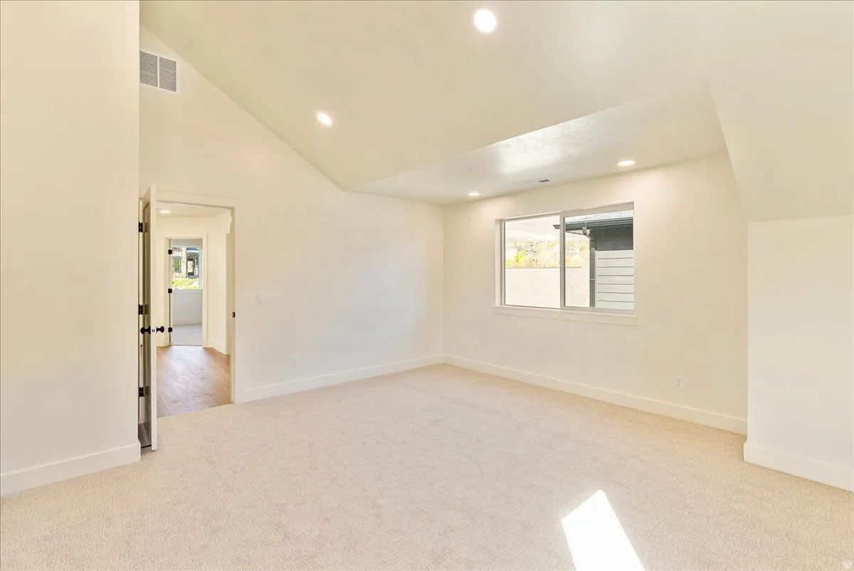 Spacious room featuring vaulted ceilings, recessed lighting, and a large window with white trim