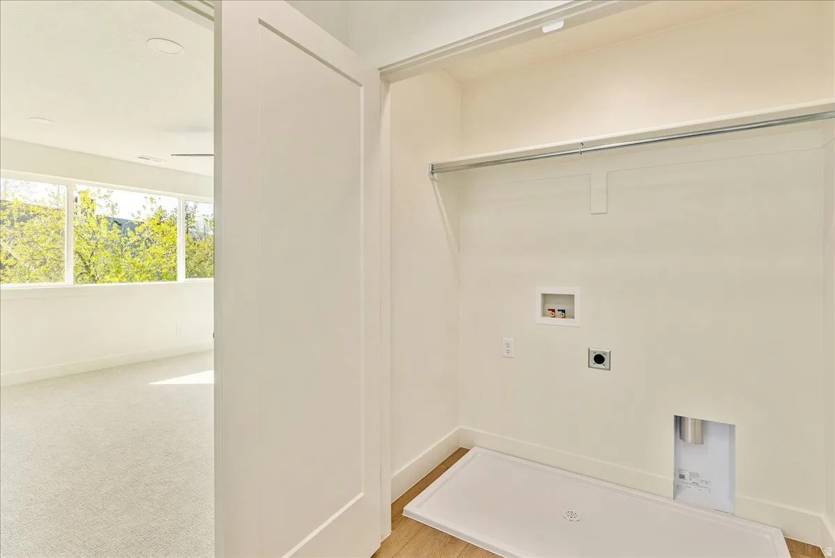 Dedicated laundry alcove with a built-in hanging rod, utility hookups, and a drain pan