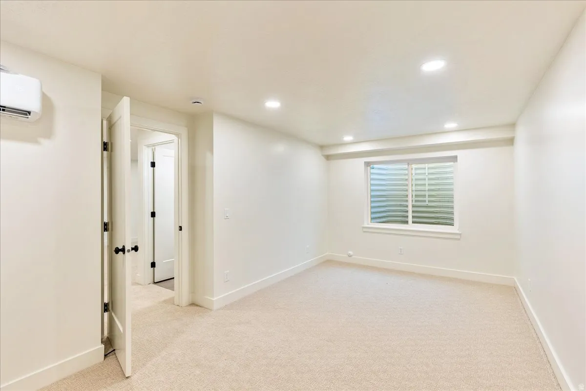 Spacious room featuring neutral carpet flooring, recessed lighting, a horizontal sliding window, a wall-mounted mini-split unit, and a paneled interior door with matte black hardware