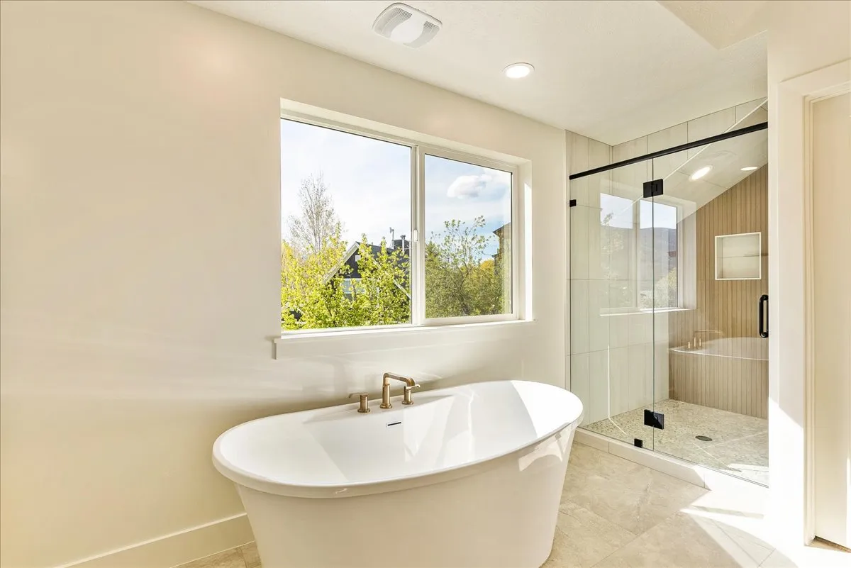 Spacious bathroom featuring a freestanding soaking tub with brass fixtures, a walk-in glass-enclosed shower with a built-in bench, and light-toned tile flooring