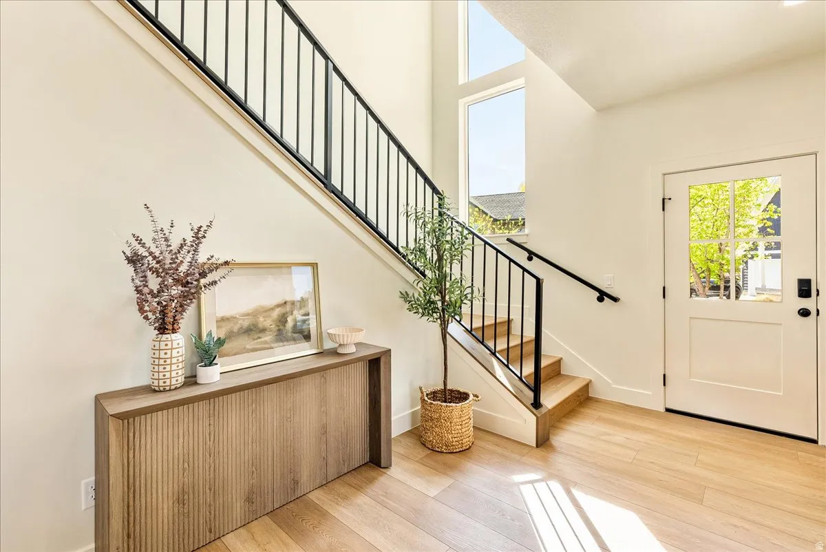 Foyer featuring a light wood-finish flooring, a white paneled door with window panes, and a modern staircase with wood treads and black metal railing