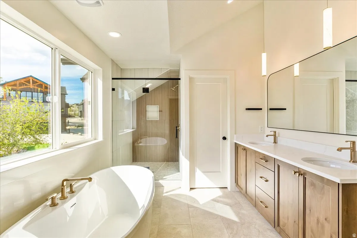 Modern bathroom featuring a freestanding soaking tub with gold-tone fixtures, a spacious glass-enclosed shower, dual vanity with wood-finish cabinetry and white countertops, a large frameless mirror, and recessed lighting