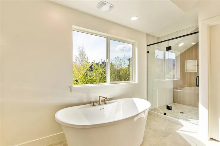 Spacious bathroom featuring a freestanding soaking tub with brass fixtures, a walk-in glass-enclosed shower with a built-in bench, and light-toned tile flooring
