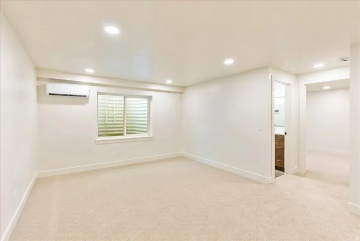 Cream-toned carpeting in a spacious room featuring a window with security grating
