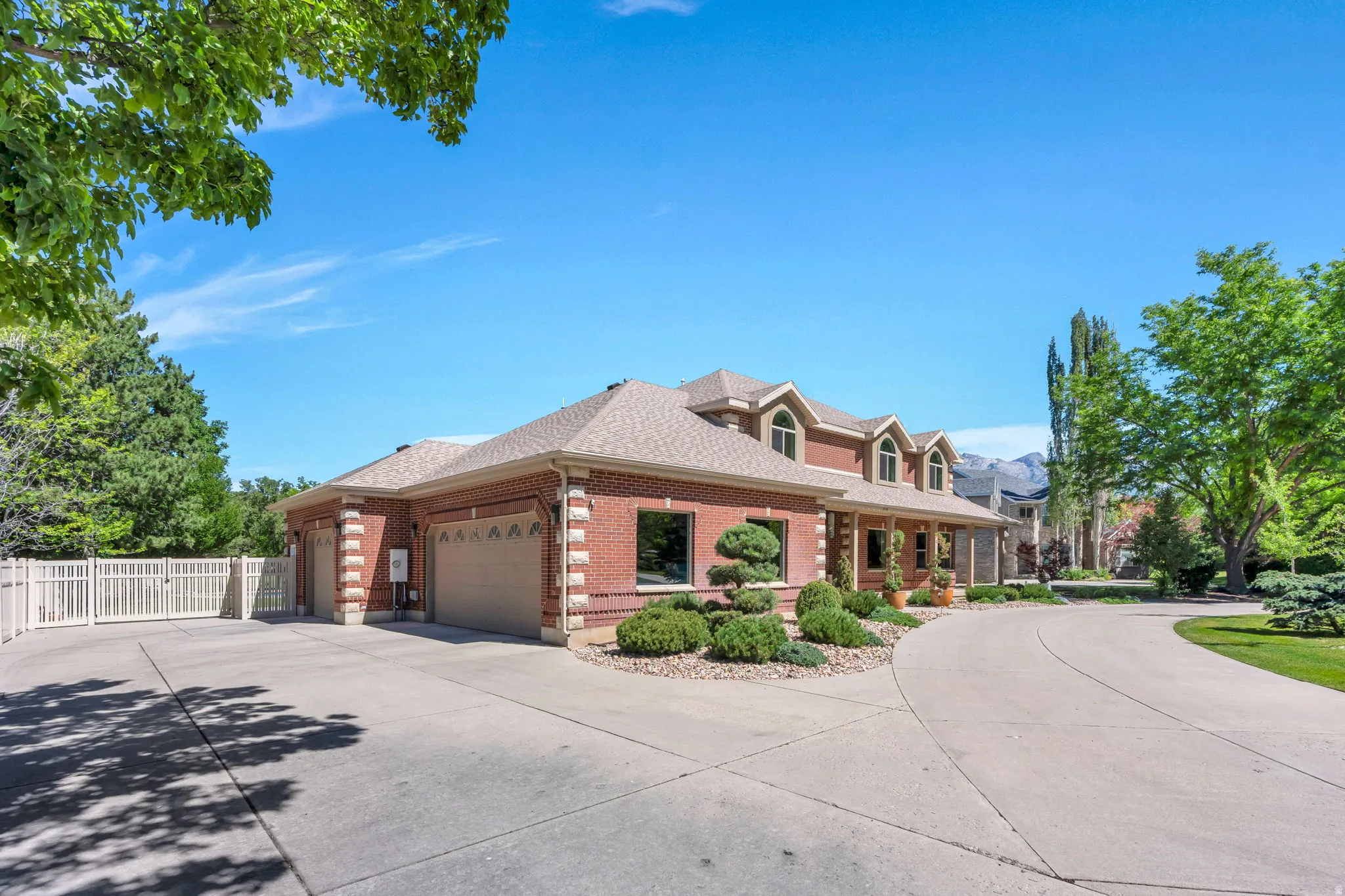 Brick exterior residence with a multi-car garage, circular driveway, arched dormer windows, and established landscaping