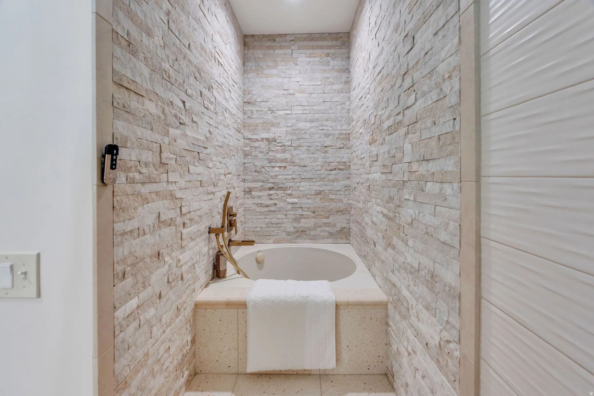 Recessed soaking tub with surrounding stone-finish decking, set within a textured stacked stone accent wall